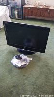 LG 32 inch television on green carpet with remote and cables wrapped in plastic bags in front.