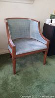 Full front view of the barrel chair showing blue fabric upholstery and wooden frame on green carpet.