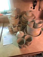 Wide view of stacked white ceramic plates, bowls, mugs, pitchers and cups with subtle ribbed texture and yellow stripes.