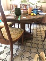 View of the dining table from the side showing one wooden chair with patterned upholstery and the double pedestal support base styled like Greek columns.