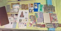 Overview photo showing multiple stacks and collections of United States stamps, first day covers, album books, and loose stamps on a flat surface.