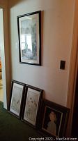 Photo showing one large framed wall art print hung on wall and three smaller framed prints resting against the baseboard.
