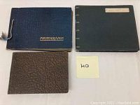 Three closed photo albums displayed on a white surface: black with string, gray with label 'Belgium 1952,' small brown textured album.