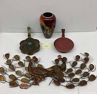 Overview of all items in the lot showing the two tin silent butlers, the vase, and the peacock metal wall hanging.