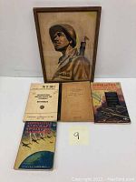Photo of a framed watercolor painting of a US Marine soldier, signed by the artist, alongside three military aviation manuals with worn covers.