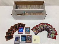 Box filled with large quantity of Yu-Gi-Oh! trading cards, with several individual cards spread in front.