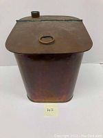 Front view of the antique copper moonshine still tub showing the tapered rectangular copper container with hinged lid and ring handle.