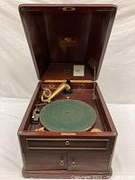 Open view of the Victrola phonograph showing wooden cabinet interior, green felt turntable and brass tonearm.