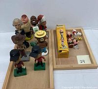 Photo showing various bobble heads including cartoon characters and sports figures placed on wooden trays.