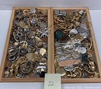 Two wooden trays filled with assorted gold-tone and silver-tone metal jewelry components including pendants, charms, and connectors arranged loosely.
