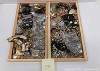 Wide view of two wooden trays filled with assorted costume jewelry pieces including earrings, brooches, bracelets, and loose components.