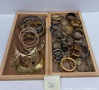 Wooden tray with two sections filled with assorted gold-tone and silver-tone choker necklaces and bracelets, showing various thin bangles and mesh style chokers.