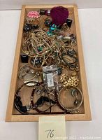 Wide angle photo showing full assortment of costume jewelry displayed on wooden tray, highlighting varied styles and colors.