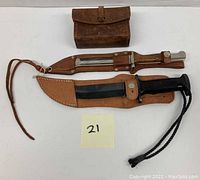 Photo showing two military fixed blade knives with sheaths and a brown leather army pouch.