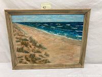 Framed oil painting depicting an ocean beach with dunes and waves.