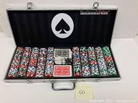 Open metal case showing organized stacks of poker chips with Trademark Poker logo on interior lid