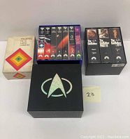 Polaroid SX-70 Land Camera box, Star Trek VHS tape sets, and The Godfather trilogy VHS tapes arranged on table.