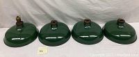 Four green enamel industrial light shades arranged in a row showing their exterior surface and metal fittings.