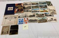 Photo showing a collection of vintage postcards, two books, and airline and railway tickets arranged on a surface.