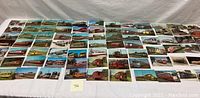 Wide view of approximately 40 vintage railway transportation postcards laid flat, showing a variety of trains, streetcars, and rail stations in color lithograph style.