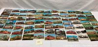 Full spread view of about 52 assorted vintage railway transportation postcards and lithographs laid out on a table.