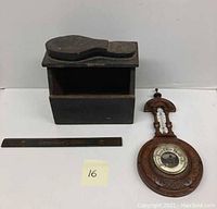 Photo showing the wooden shoeshine box, the wooden wall mounted barometer, and the Paramount Pictures measuring ruler placed on a white background.