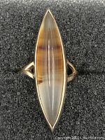Top-down view of elongated marquise-shaped agate stone set in 10Kt gold ring against black textured background.