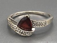 Close-up front angle showing the triangular red garnet, diamond accents on one side of the band, and 10Kt white gold band with light wear.