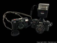 Two Ricoh cameras with a Starblitz 200 DNX external flash, camera straps attached, on black background