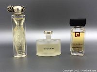 Three perfume bottles displayed side by side: tall Caron Parfum bottle, frosted Bvlgari bottle, small Paco Rabanne bottle with amber liquid.