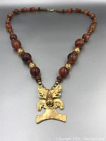 Full view of the necklace showing round agate beads strung with small gold-tone beads and large ornate gold-tone pendant.