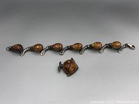 Photo of vintage amber bracelet with six teardrop amber segments and fish-shaped amber brooch together on gray background.