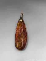 Front view of the teardrop-shaped amber pendant showing its internal inclusions and translucent amber colors.