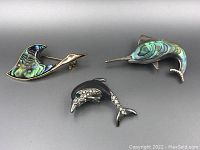 Photo of three animal brooches showing swordfish and dolphin with shell inlay and a black dolphin with rhinestones.