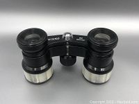 Front angled view showing black metal frame, central adjustment knob, and mother of pearl inlay on the barrels.