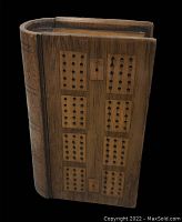 Front view of the cribbage board showing peg holes arranged in groups on wooden surface and a carved book spine.
