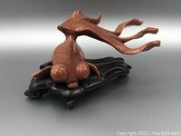 Front angled view of the reddish goldstone fish sculpture with bulging eyes and long fins on a black carved stand.