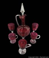 Full set of cranberry glass decanter and six matching glasses, three with handles and three without, displayed against a black background showing all items.