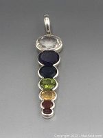Front view of pendant showing clear quartz, amethyst, a deep blue stone, peridot, citrine and two red garnet stones all bezel set in sterling silver.