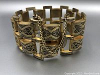 Close-up front view showing engraved decorative patterns on the interlocking rectangular links of the bracelet along with the safety chain clasp.