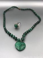 Photo showing full necklace with graduated malachite beads, heart-shaped malachite pendant, and silver ring with oval malachite and decorative stones.