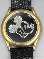 Close-up of vintage Mickey Mouse watch face with gold-tone casing and black textured leather strap. Gemstone and glitter details on Mickey Mouse face visible, showing signs of wear and scratches.