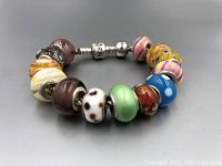 Full view of silver Pandora bracelet with the 13 assorted glass beads in various colors and designs arranged around it.