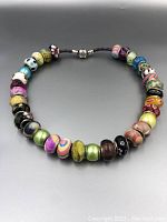 Overview of the silver Pandora necklace arranged in a circular form displaying all 33 multicolored glass beads with varied patterns.