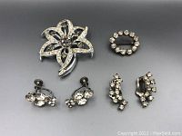 Two rhinestone brooches and two pairs of clip-on rhinestone earrings arranged against a dark background