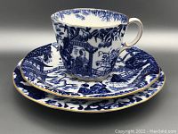 Teacup, saucer, and plate with blue and white oriental design and gold edges arranged stacked on gray background