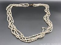 Top view photo of the full 4-strand seed-pearl necklace on dark gray background showing shape and clasp.