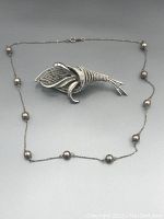 Silver-tone chain necklace with spherical beads paired with floral motif Coro brooch, displayed on gray background.