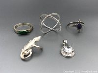 Top-down view of 3 rings, pendant, and alligator toe ring laid out on gray surface