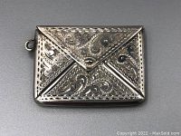 Front view of the sterling silver stamp holder showing engraved floral and scroll designs and side loop.